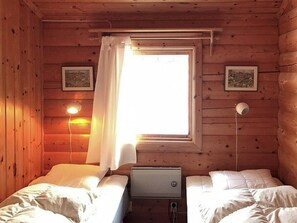 Une cabine avec deux lits, une fenêtre avec des rideaux et des lampes fixées au mur.
