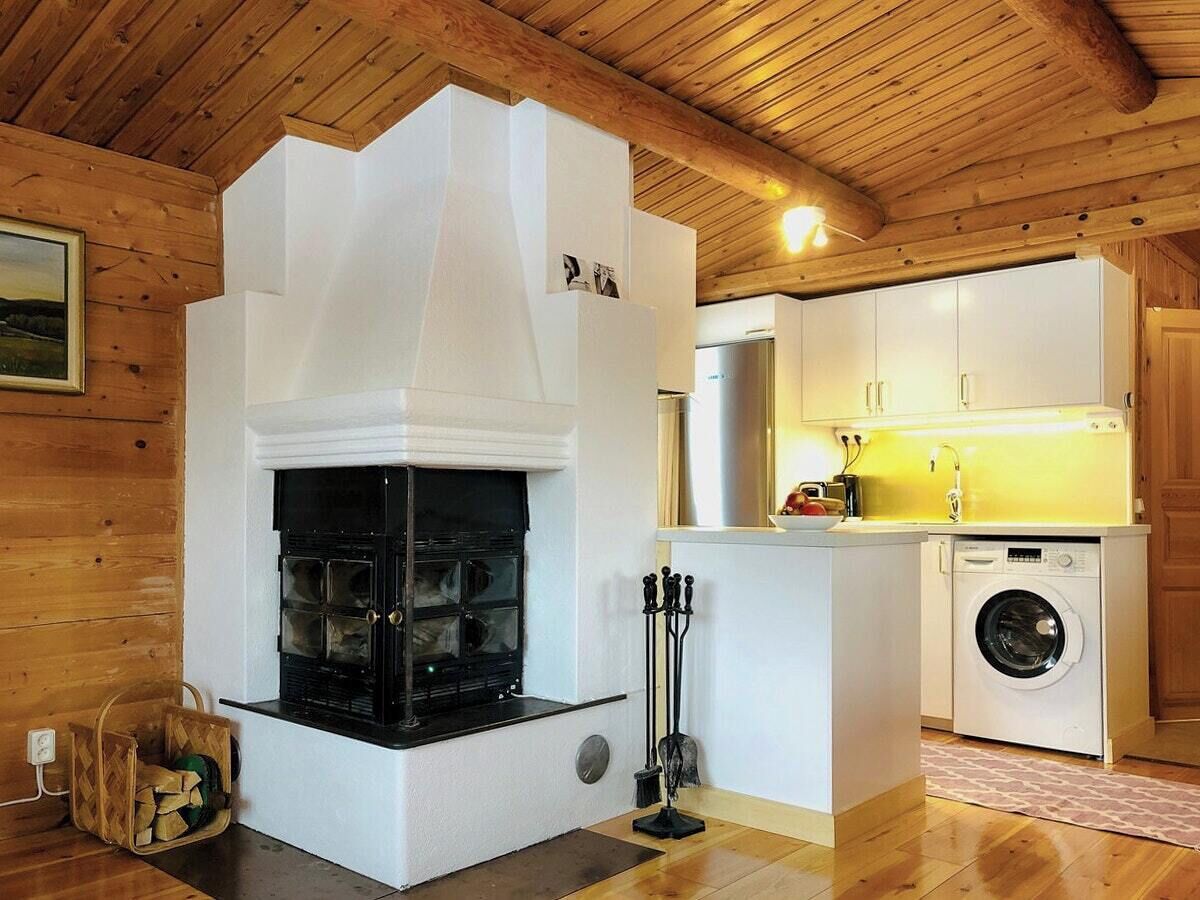 Interior de madera con chimenea, lavadora y zona de cocina.