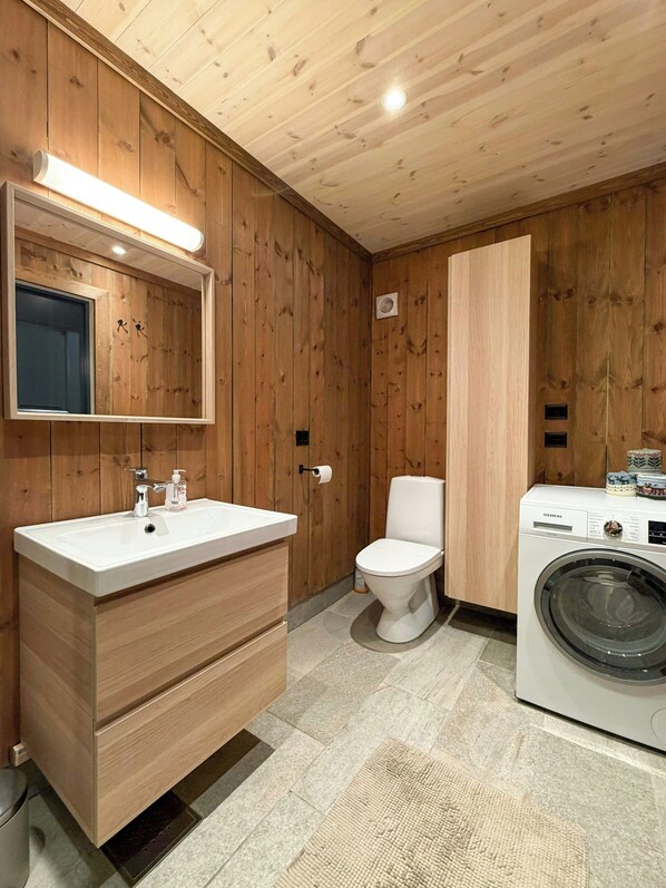 A wooden-paneled bathroom with a sink, toilet, and washing machine.