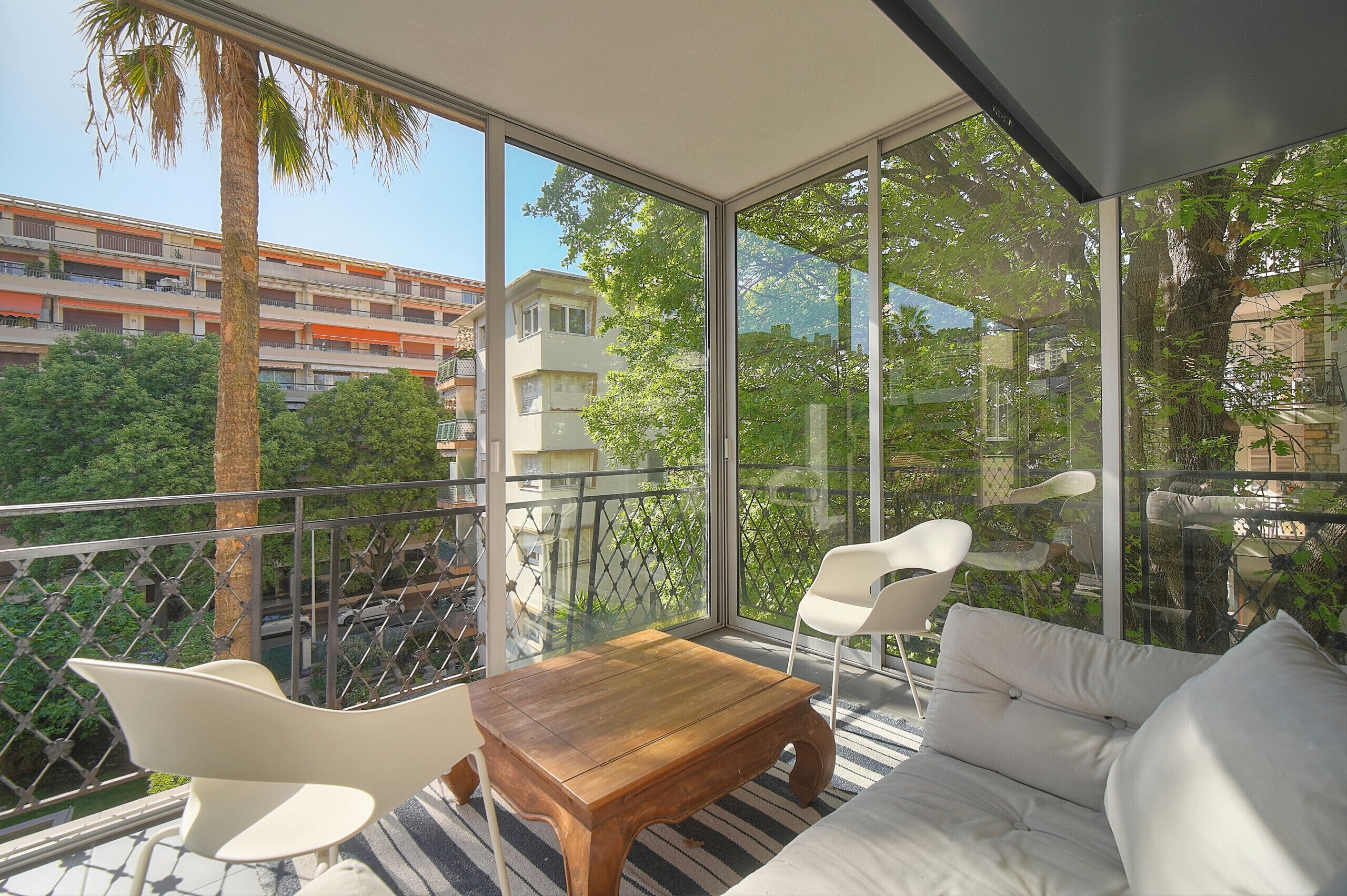 Un balcon avec une table en bois, des chaises blanches et un canapé.