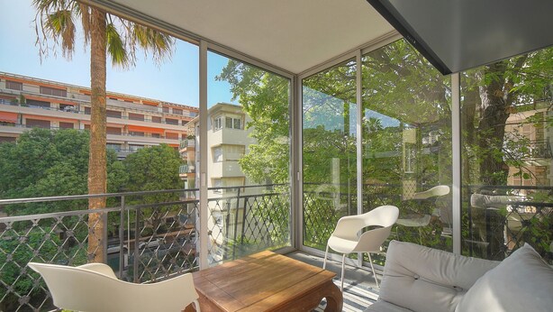 Ein Balkon mit Holztisch, weißen Stühlen und einer Couch.