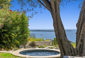 A hot tub surrounded by greenery and a view of the sea.