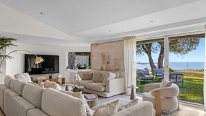 A modern living room with a large flat-screen TV, beige sofas, a coffee table, and a view of the sea through large windows. - FRGK Luxury Sea View Villa ANITA Heated Pool 7 Bed (Cannes)