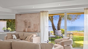 A modern living room with a large window, a sofa, a coffee table, and a view of the sea. - FRGK Luxury Sea View Villa ANITA Heated Pool 7 Bed (Cannes)