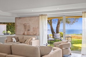 A modern living room with a large window, a sofa, a coffee table, and a view of the sea.