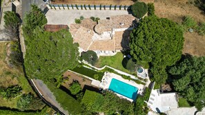 An aerial view of a residential property with a swimming pool, a patio area, and a large lawn.