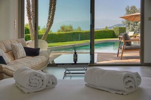 A room with a large sliding glass door leading to a pool area, a sofa, a coffee table, and towels on the floor.