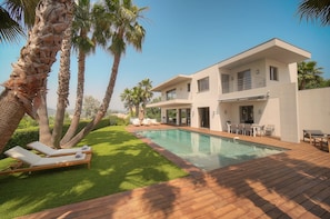 Une maison moderne à deux étages, dotée d’une piscine, de mobilier d’extérieur et de palmiers.