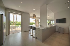 Une cuisine moderne dotée d’un grand îlot central, de tabourets de bar et d’un coin repas avec des sièges à l’extérieur.