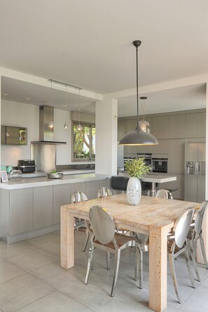 Une cuisine moderne dotée d’un îlot central, d’appareils électroménagers en acier inoxydable et de luminaires suspendus.