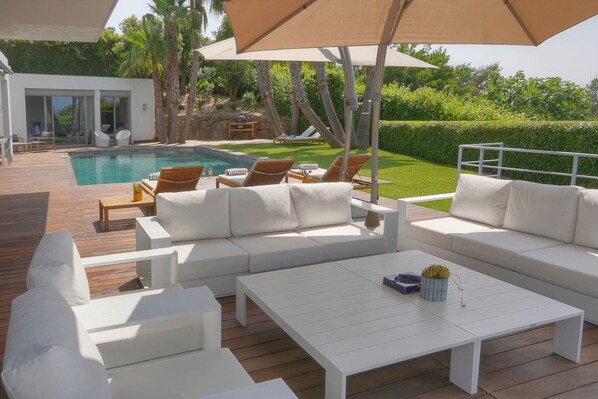A poolside area with a white sofa, a white coffee table, and a large umbrella.