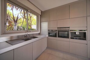 A modern kitchen with a built-in oven, a sink, and a window with a view of greenery.