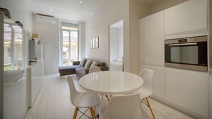 Eine moderne Küche mit weißen Schränken, einem eingebauten Ofen und einem Essbereich mit einem weißen Tisch und Stühlen.
