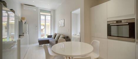 A modern kitchen with white cabinets, a built-in oven, and a dining area with a round table and chairs.