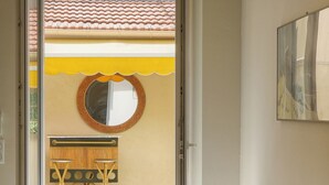 Ein modernes Wohnzimmer mit einem grauen Sofa, einem runden Spiegel und Blick auf eine Terrasse mit einem Holztisch und Stühlen.