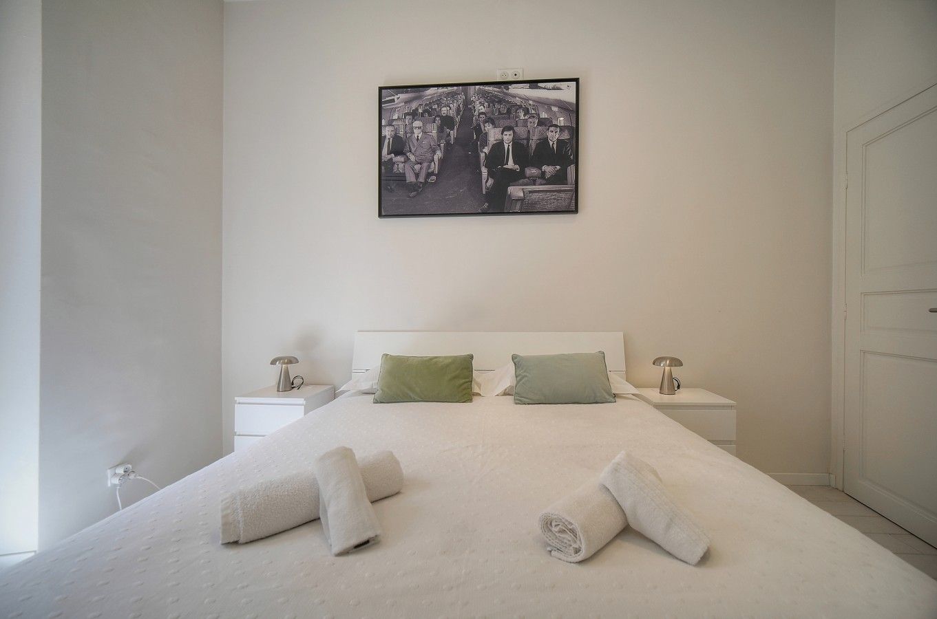Habitación de hotel con una cama grande, dos mesitas de noche, un cuadro colgado en la pared y una puerta.