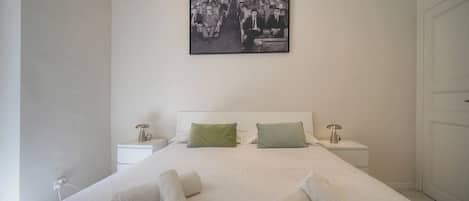 Habitación de hotel con una cama grande, dos mesitas de noche, un cuadro colgado en la pared y una puerta.