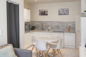 Una cocina moderna con armarios blancos, una mesa redonda de comedor con sillas blancas y dos fotografías blanco y negro en la pared.