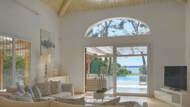 A spacious living room with a large sofa, a flat-screen TV, and a view of a pool and outdoor seating area. - FRGK Villa Mare Moure Rouge Palm Beach (Cannes)