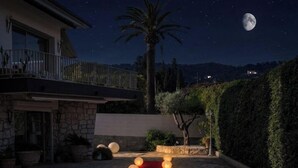 Uma área externa iluminada à noite, com um tapete vermelho que conduz a um edifício, decorada com luzes esféricas sob um céu noturno com a lua visível.