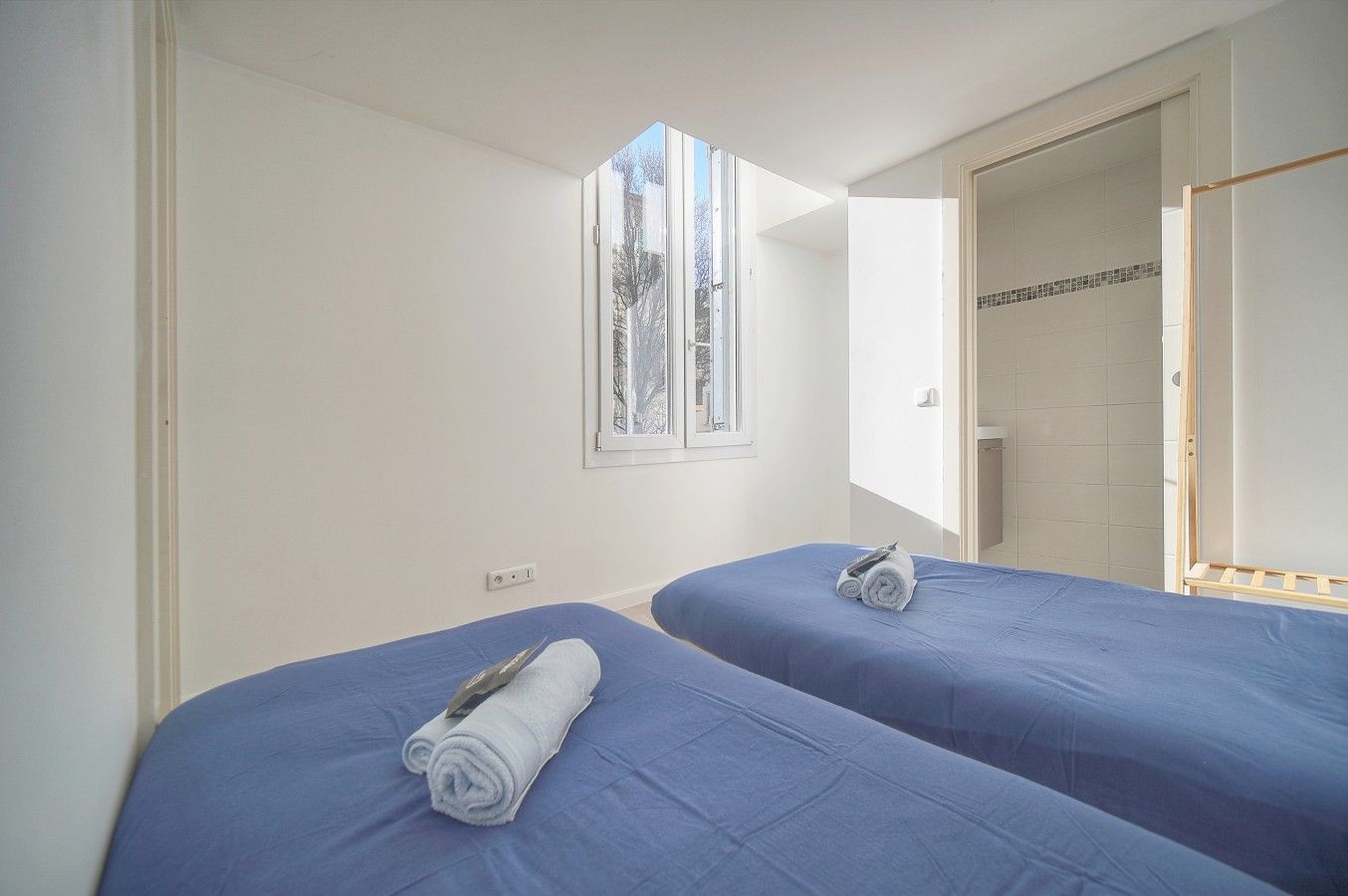 A room with two beds, a window, and a door leading to a bathroom.