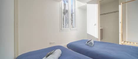 Una habitación con dos camas, una ventana y una puerta que da a un baño.