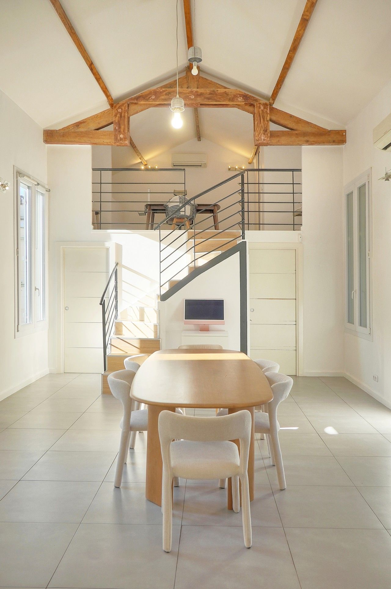A spacious room with a high ceiling, a wooden staircase, a dining table with chairs, and a television.