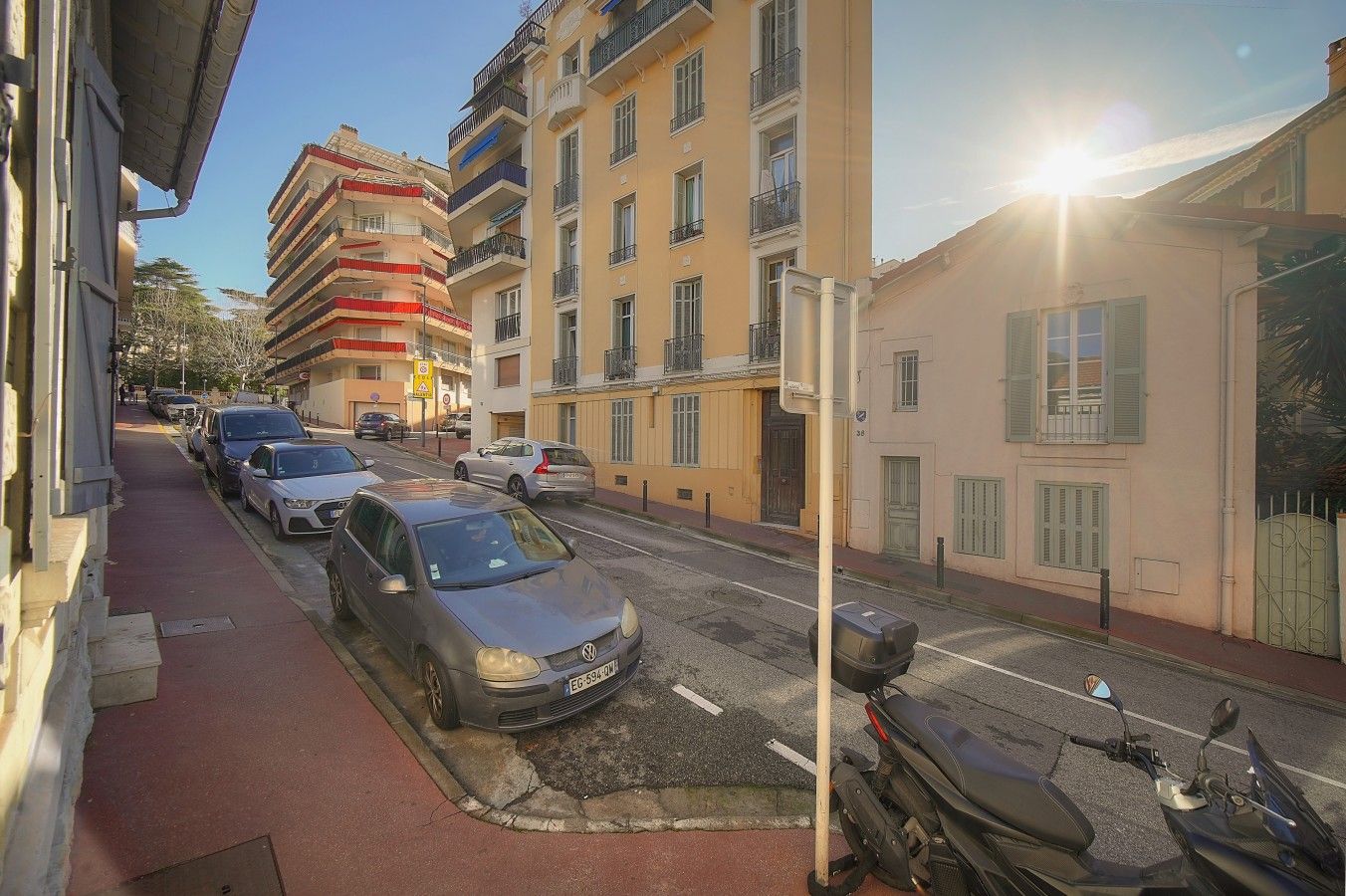 Una strada con auto parcheggiate e un palazzo con balconi.