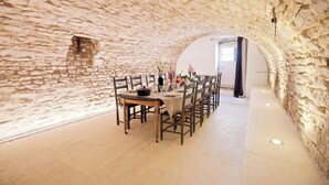 Een eetruimte met een stenen muur, een ronde tafel gedekt voor zes personen en een uitzicht door een boogvormige doorgang.