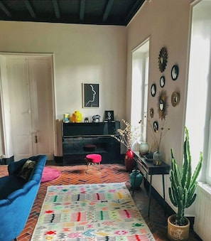 Ein Wohnzimmer mit Klavier, einem blauen Sofa, einem gemusterten Teppich und einer Kakteenpflanze.