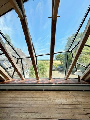 A room with a sloped ceiling and large windows, wooden beams, and a view of a green landscape. - Artist's house in first row by Smålandshavet (Horslunde)