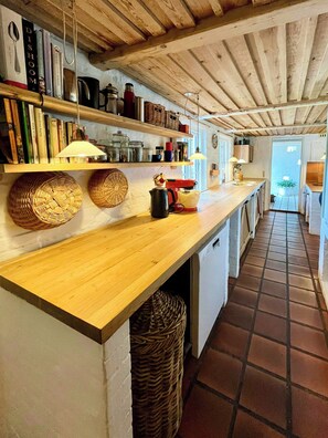 A kitchen with wooden shelves, a long counter, and a tiled floor. - Artist's house in first row by Smålandshavet (Horslunde)