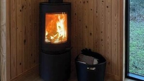 A wood-burning stove in a corner with wooden walls and a window. - Newly renovated holiday home near Torndal beach (Hals)