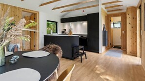 A modern kitchen with wooden beams, a dining area with a round table, and a view of the outdoors. - Newly renovated holiday home near Torndal beach (Hals)