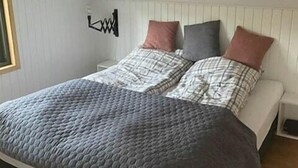 A bed with a quilted cover, a bedside table, and a wall-mounted light fixture. - Newly renovated holiday home near Torndal beach (Hals)