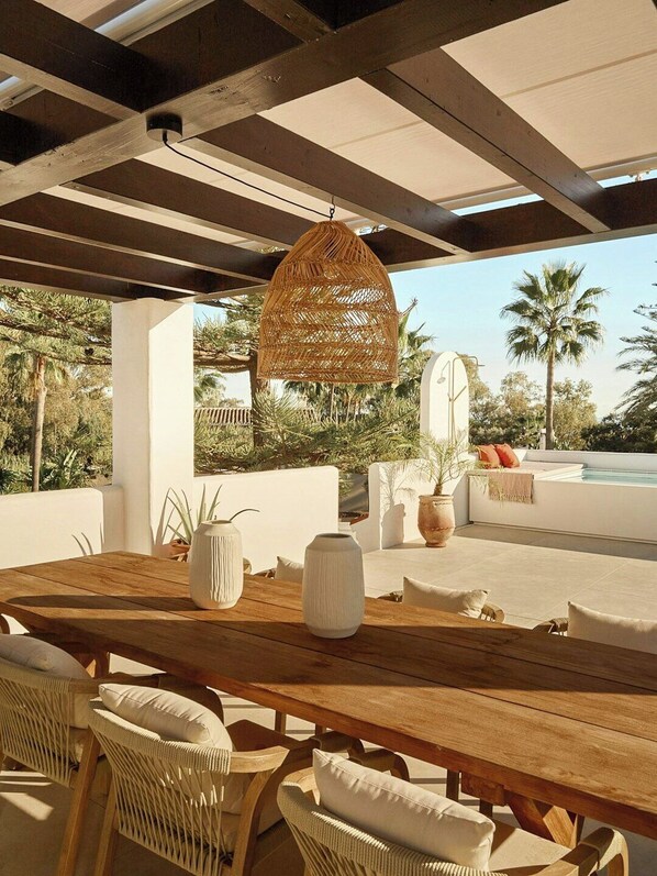 An outdoor dining area with a wooden table, wicker chairs, and a hanging rattan light fixture. - Villa with rooftop terrace near beach in Marbella (Marbella)