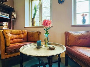 A room with a brown leather sofa, a round table with a decorative tray, and a window with a potted plant. - Authentic farm close to the water on Samsø (Samsø)