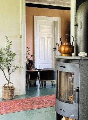 A room with a fireplace, a table with chairs, a potted plant, and a door. - Authentic farm close to the water on Samsø (Samsø)