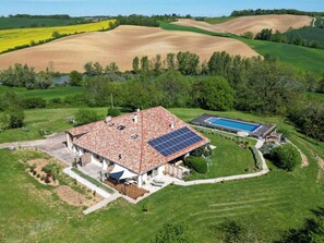 Ein Haus mit einem Ziegeldach, einem Swimmingpool und Solaranlagen.