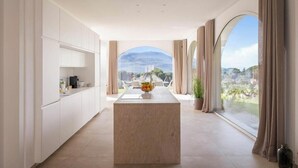 A modern kitchen with a marble island, white cabinetry, and a view through large windows. - Historic villa overlooking Scopello sea stacks (Castellammare del Golfo)