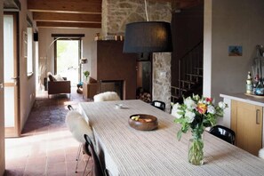 A dining area with a long table, chairs, a vase with flowers, and a fireplace. - Stone house in Piedmont with infinity pool (Cossano Belbo)