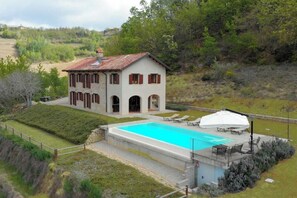 A two-story house with a swimming pool, a covered patio, and a garden. - Stone house in Piedmont with infinity pool (Cossano Belbo)