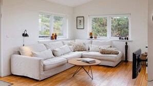 A modern living room with a sectional sofa, a round coffee table, and a television. - Enjoy the sound of crashing waves and ocean views (Græsted)