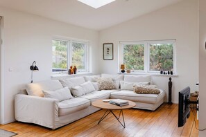 A modern living room with a sectional sofa, a round coffee table, and a television. - Enjoy the sound of crashing waves and ocean views (Græsted)