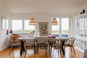 A dining area with a wooden table, wicker chairs, and pendant lights. - Enjoy the sound of crashing waves and ocean views (Græsted)