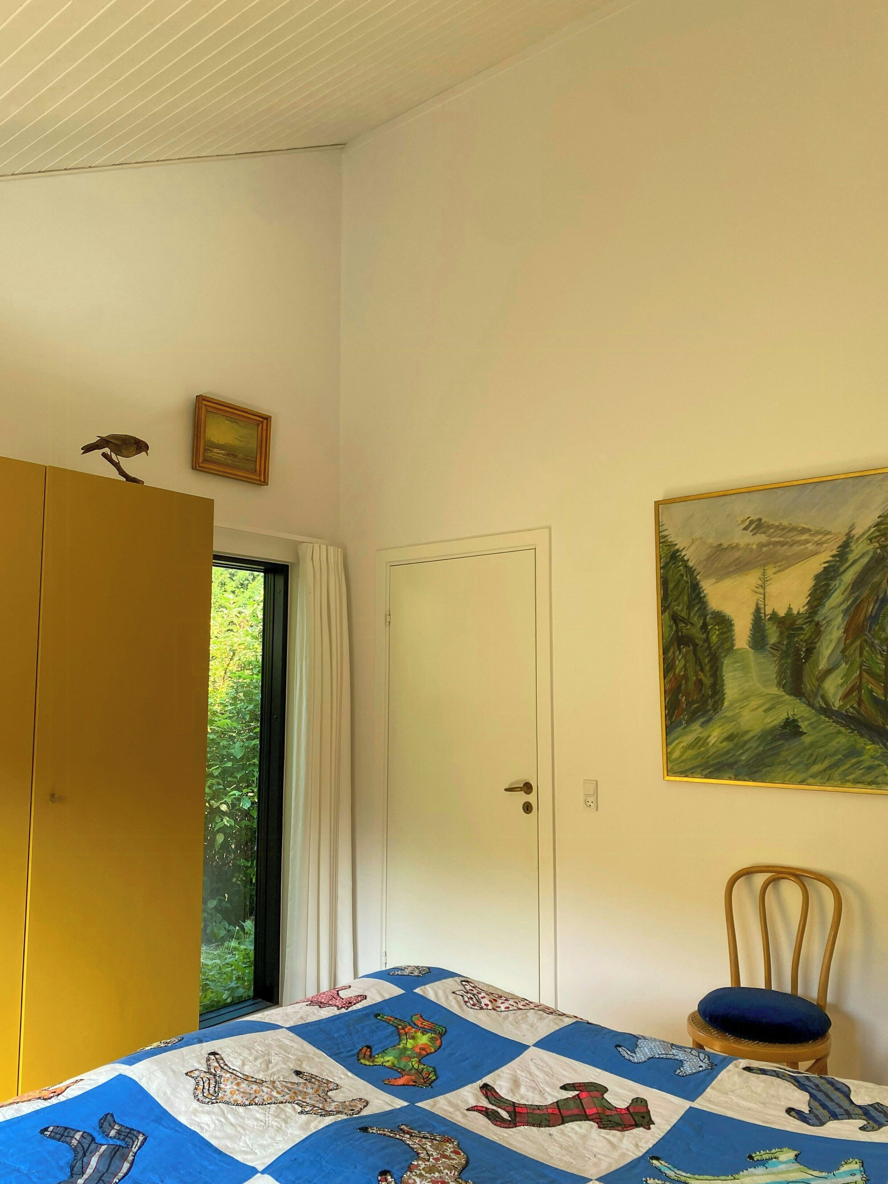Ein Schlafzimmer mit Bett, Kleiderschrank, Tür, einem Bild und einem Sessel.