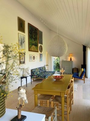 A dining area with a wooden table and chairs, a sofa, and wall art. - Artistic holiday home near Tisvilde Hegn (Vejby)