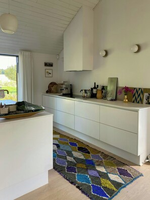 A modern kitchen with white cabinetry, a patterned rug, and a view of the outdoors. - Artistic holiday home near Tisvilde Hegn (Vejby)