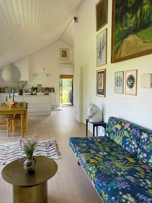 A spacious living area with a sofa, a dining table, and a kitchen in the background. - Artistic holiday home near Tisvilde Hegn (Vejby)