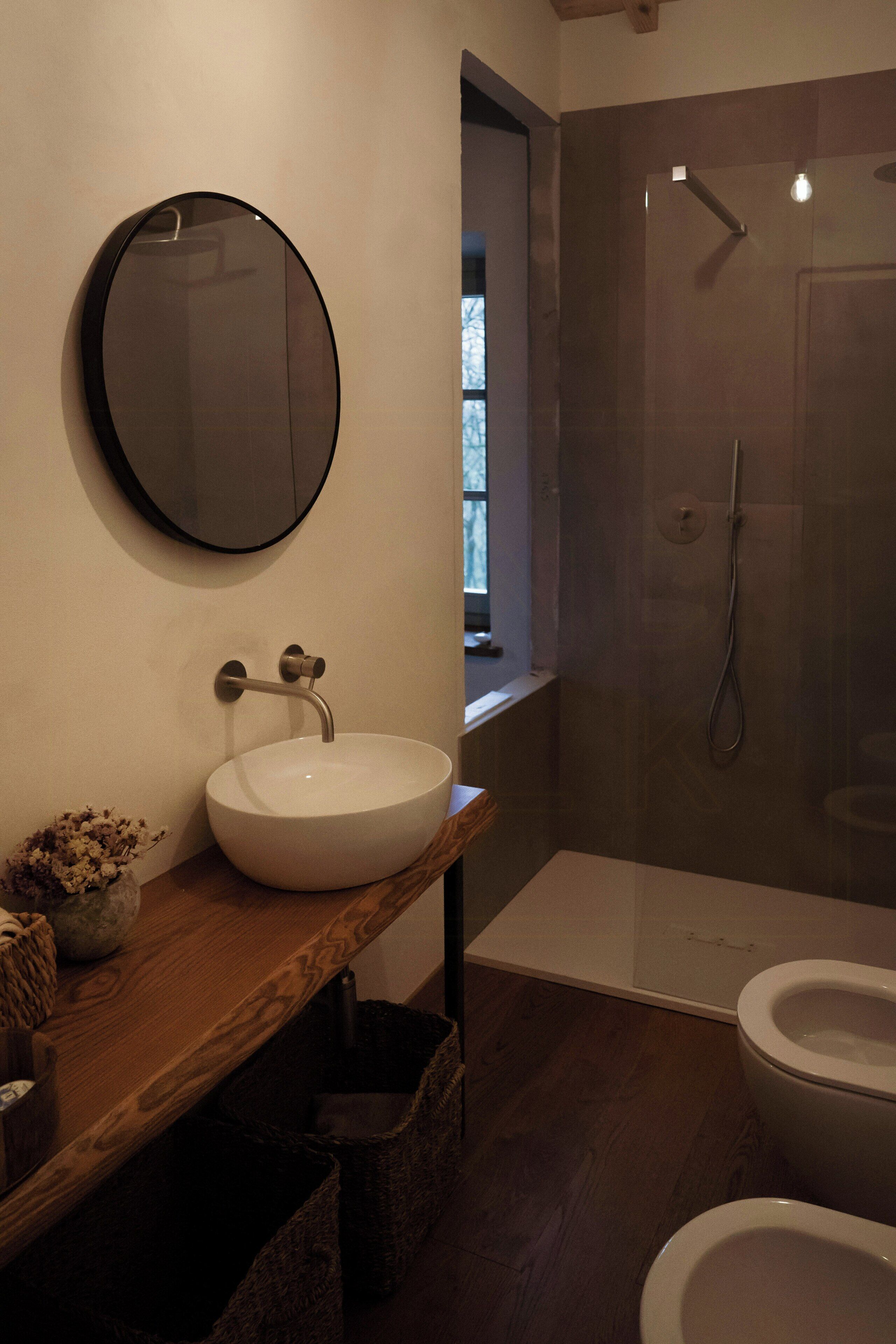Ein Badezimmer mit rundem Spiegel, Waschbecken in Weiß, Dusche und Toilette.